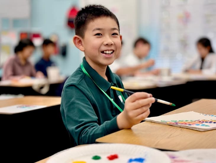 A student smiling while painting during Young Artists Day