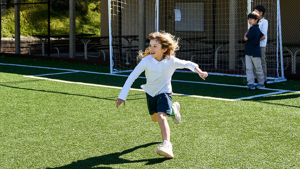 A student running and laughing on the field during outdoor play