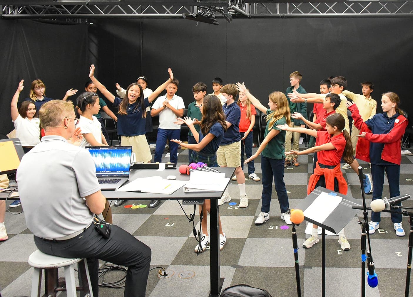 A teacher leading students in a music and movement rehearsal on stage