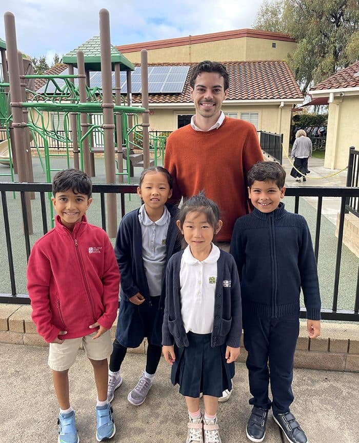 Students and a teacher outside beside the school's gated, fenced playground