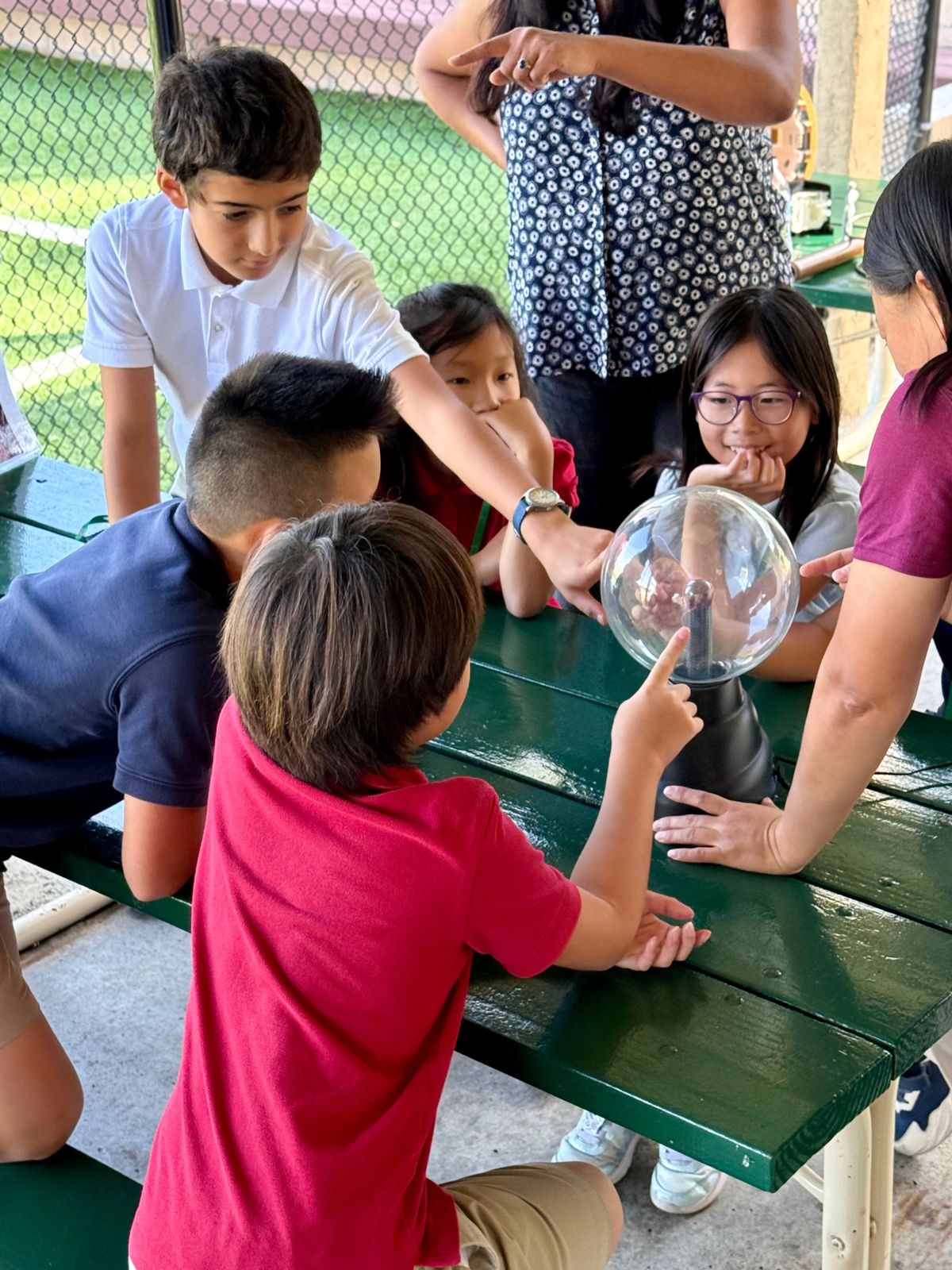 Students gathered around a plasma globe on a picnic table, reaching out to touch the glass.